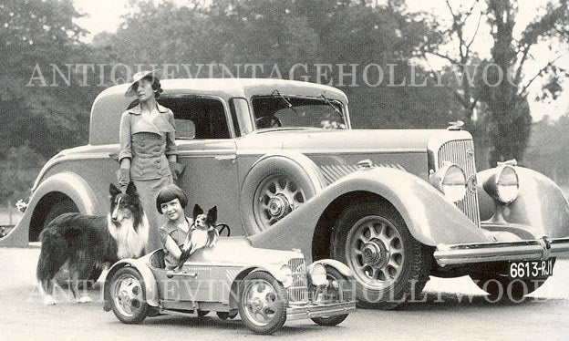 Mrs. Cow (wife of artist Alexis Cow) with her daughter, their dogs (a collie and a papillon), and a Eureka children's pedal car, 1934. A Panhard & Levassor car is visible in the background. A00013