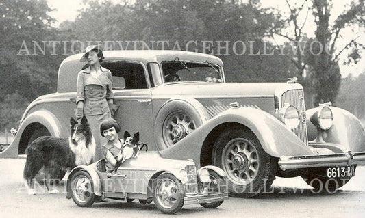 Mrs. Cow (wife of artist Alexis Cow) with her daughter, their dogs (a collie and a papillon), and a Eureka children's pedal car, 1934. A Panhard & Levassor car is visible in the background. A00013